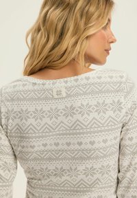 Długi rękaw bluzka w jasnoszarym kolorze z dzianinowym wzorem w gwiazdki i zygzaki. Materiał jest miękki, z okrągłym dekoltem i małą metką.