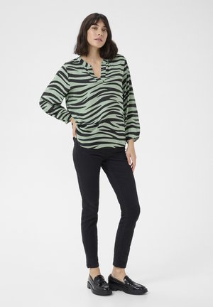 Green and black zebra-striped blouse with a V-neckline, long sleeves, and a relaxed fit, paired with black skinny pants and glossy shoes.
