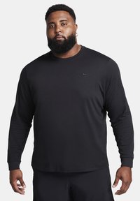 Long-sleeve black shirt with a round neckline, made of soft fabric. Features a small Nike logo on the left chest. Casual fit design.