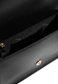 Interno di una borsa in pelle nera con scomparto con zip, texture liscia e chiusura a scatto dorata. Dettaglio di fodera sottile visibile.