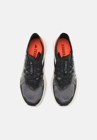 Black and gray athletic shoes with a mesh upper, featuring a white logo, and an orange insole. The design includes laces and textured panels.