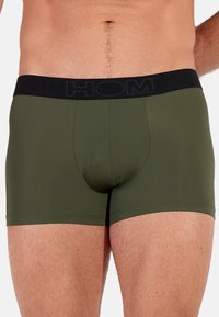Boxer in verde oliva scuro, realizzati in tessuto morbido. Dotati di una cintura elastica nera con il nome del marchio 'HOM' in evidenza.