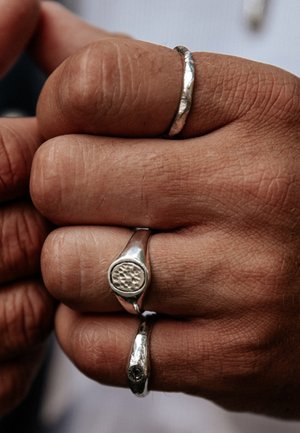 Gros plan d'une main avec trois bagues en argent, une alliance martelée sur l'index et deux bagues à motifs sur le majeur et l'annulaire.