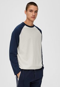 Langärmliges Shirt mit Raglanärmeln in Creme und Marine, mit Rundhalsausschnitt, weichem Stoff und lockerer Passform. Kombiniert mit dunklen Hosen.