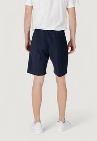 Pantaloni corti blu navy con vita elastica, due tasche posteriori e taglio dritto. Indossati con scarpe da ginnastica bianche su uno sfondo neutro.