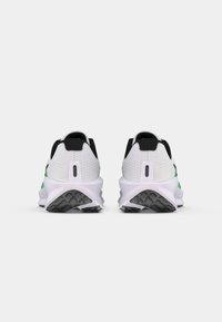 Black and white athletic shoes with green accents; mesh upper, padded heel, and textured black rubber sole. Rear view shows logo detail.