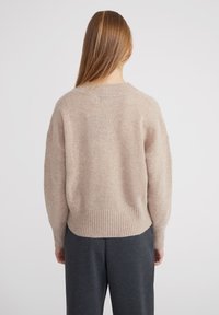 Maglione beige, strutturato, con orlo e polsini a coste, caratterizzato da una vestibilità ampia e maniche larghe. Indossato su pantaloni grigi scuri.