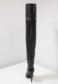 Botte en cuir noir, haute jusqu'au genou, à bout pointu, avec un talon aiguille et une texture lisse. Comprend un accent de fermeture éclair sur le côté.
