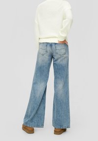 Szerokie niebieskie dżinsy z jasnym praniem. Posiadają tylne kieszenie i lekko wyblakłą teksturę, w połączeniu z białym swetrem z dzianiny.