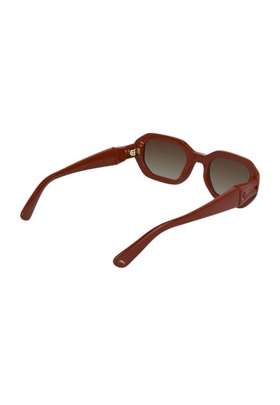 Lunettes de soleil en plastique rouge avec une monture octogonale, des verres marron dégradés et des branches allongées. Dotées d'un subtil détail en métal doré sur le côté.