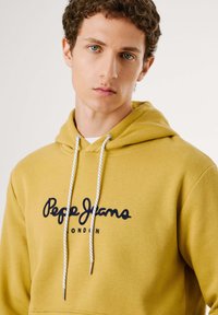 Mustard yellow hoodie with a front pocket, white drawstrings, and dark blue "Pepe Jeans" logo on the chest, made from soft fabric.