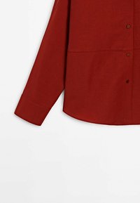 Chemise boutonnée à manches longues rouge foncé avec des boutons marron visibles et un poignet simple sur fond blanc.