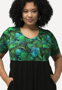 Vestido negro con mangas cortas que presenta un patrón de hojas tropicales en verde y azul en la parte superior y una sección inferior de tela negra fruncida.