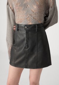 Black leather mini skirt with a fitted design, featuring a front seam, button closure, and belt loops. Pairing with a knitted, openwork top.