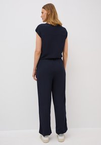 Marineblauwe jumpsuit met korte mouwen en elastische tailleband, met een relaxte pasvorm en rechte pijpen. Gekocht met lichte sneakers.