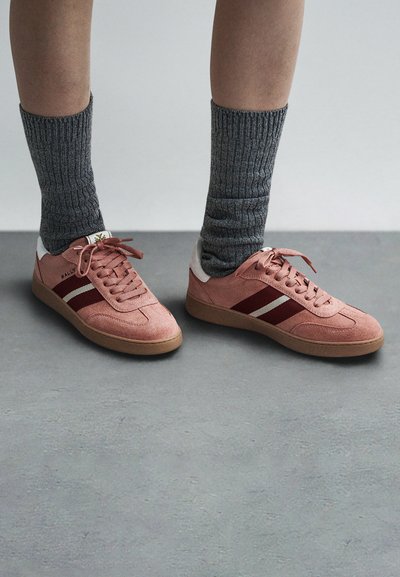 Rosa semskesko med burgunderstriper, gummisåler og hvite detaljer. Kombinert med grå ribbestrikkede sokker.