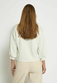 Light cream, pullover top with a round neckline and balloon sleeves. Soft texture, cropped length, paired with beige, high-waisted pants.