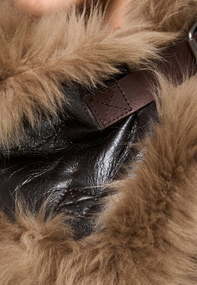 Fodera in pelliccia marrone soffice che circonda un materiale in pelle marrone scuro, con una cinghia di pelle cucita e dettagli in fibbia metallica.