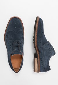 Chaussures brogues en daim bleu marine avec design à bout golf, détails perforés et accents en cuir brun ; semelle en caoutchouc légère assurant une bonne adhérence.
