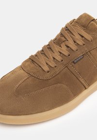 Sneaker in suede marrone con tomaia texture, punta rotonda e suola in gomma beige. Presenta lacci tonali e un marchio laterale.