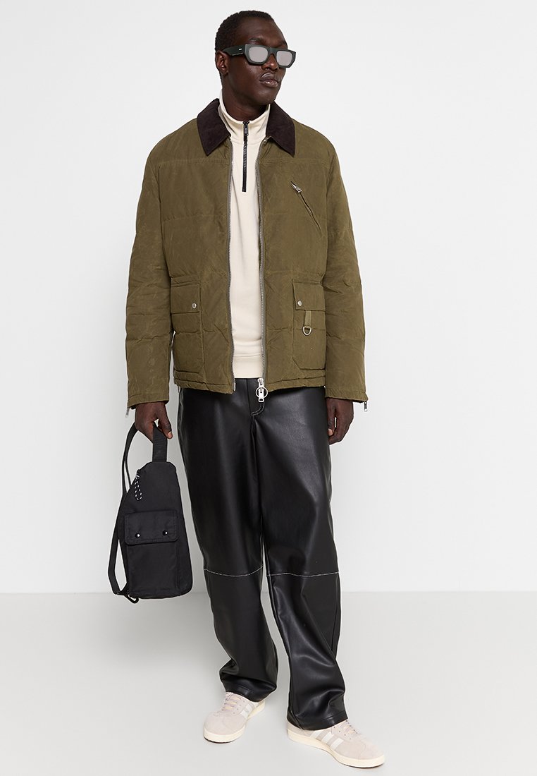 Zielono-oliwkowa pikowana kurtka z brązowym kołnierzem, z przodu na suwak, z dwiema kieszeniami. Połączona z czarnymi spodniami z sztucznej skóry i jasnymi sneakersami.