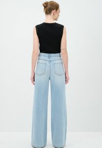 Vaqueros de pierna ancha de corte alto en un azul claro, confeccionados en denim, con bolsillos traseros y una camiseta sin mangas negra. Detalles de costura simples visibles.