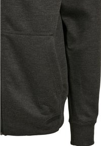 Giacca zip grigia scura con tasca frontale e polsini elasticizzati su maniche lunghe, che mostra la trama del tessuto e un'etichette del marchio vicino all'orlo.