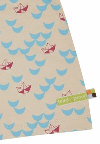 Beige stof met een herhalend patroon van lichtblauwe golven en rode papieren boten. Inclusief een groene "loud + proud" label.