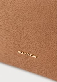 Cartera de cuero marrón texturizado con un logotipo en dorado de "MICHAEL KORS" en el frente, que muestra un diseño de superficie granulada.