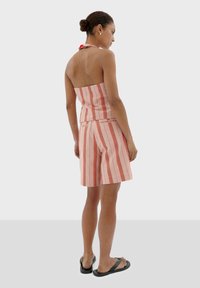 Gestreepte roze en rode haltertop met een getailleerde taille en losse short, gemaakt van lichtgewicht stof. Draag met zwarte slippers.