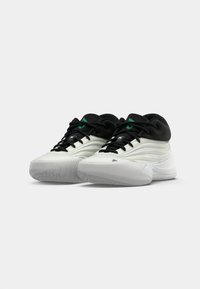 Black and white athletic shoes feature a textured upper, prominent lacing system, and green accents. The sole is designed for traction.