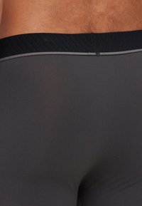 Čierne športové spodné prádlo s ribovaným elastickým pásom zdobeným šedou akcentovou líniou. Hladký, priliehavý materiál, vhodný na aktívne nosenie.