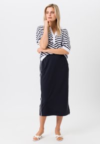 Gestreept, kort mouwend, marineblauw en wit bovenstuk met een v-hals; bijpassende marineblauwe rok met zijstrepen; witte blokhak sandalen.