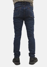 Jeans in denim blu scuro con un taglio slim, caratterizzati da tasche posteriori cucite e un'etichetta in pelle sulla vita.