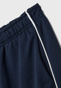 Granatowe spodenki sportowe z elastycznym pasem, z białymi bocznymi paskami i miękkim, teksturowanym materiałem.