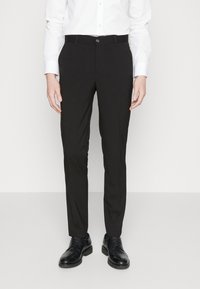Pantalones negros ajustados con un corte slim, textura suave y cierre de botón. Combinados con una camisa blanca y zapatos de vestir negros.