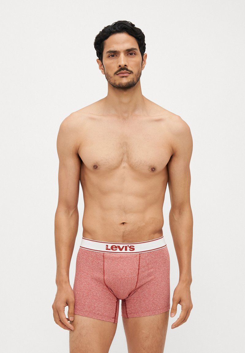 Crvene bokserice s mekim, teksturiranim materijalom i bijelim pojasom na kojem se nalazi "Levi's" logo u crvenoj boji. Duljina do sredine bedra i uski dizajn.