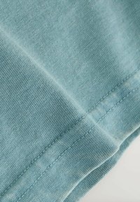 Close-up van lichtblauwe stof die een gedetailleerde gebreide textuur en dubbel gestikte naad aan de gevouwen rand toont.