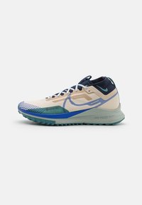Chaussure de trail Nike avec une tige beige clair et bleu marine, en mesh texturé, détail GORE-TEX, et une semelle en caoutchouc turquoise à profil épais.