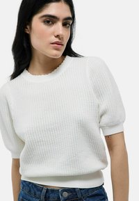 Pull blanc texturé avec un col festonné et des manches courtes bouffantes, associé à un short en denim taille haute avec un accent de bouton.