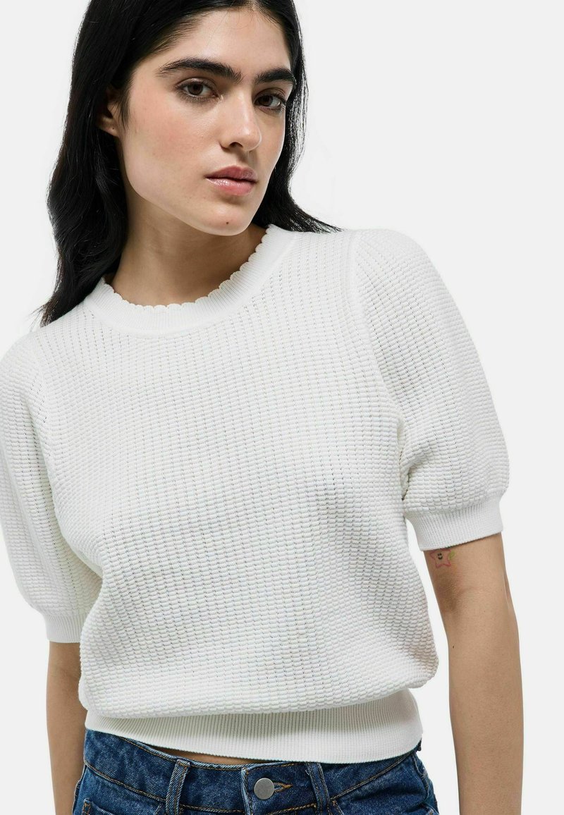 Pull blanc texturé avec un col festonné et des manches courtes bouffantes, associé à un short en denim taille haute avec un accent de bouton.