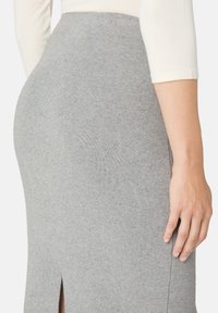 Šedá úzká pletená sukně s vysokým pasem a bočním rozparkem, zobrazená zezadu. Měkká textura a přiléhavý střih.