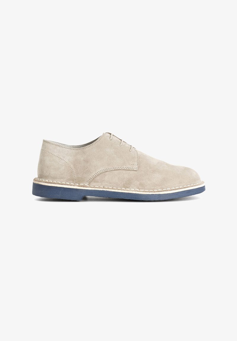 Scarpe in suede beige con punta rotonda, caratterizzate da un semplice design con lacci e una suola blu a contrasto con cuciture lungo il bordo.