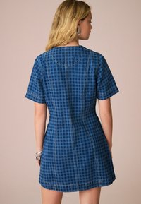Kratka denim obleka v temno modri barvi s karirastim vzorcem. Oblika v slogu črke A z vidnimi šivi in okroglo izrezom.