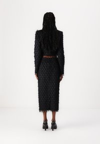 Black textured two-piece outfit featuring a cropped jacket and knee-length skirt with a layered fringe design and high-heeled shoes.