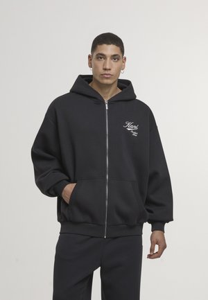 Czarna bluza z kapturem na zamek, z dużym kapturem, przednimi kieszeniami, ściągaczami przy rękawach i wyszywanym logo na piersi. Wykonana z miękkiego, grubego materiału.