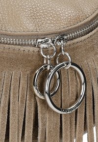 Franje tas in zacht, beige suede met een gestructureerde afwerking. Voorzien van een zilveren rits en twee ronde metalen accenten aan een ritskleur.