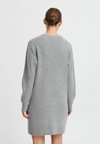 Abito grigio a maglia con texture a coste, maniche lunghe e scollatura rotonda, caratterizzato da un orlo posteriore leggermente più lungo.