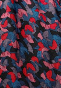 Motif abstrait sur tissu avec des formes irrégulières rouges, bleues, roses et noires sur un fond de tissu texturé.