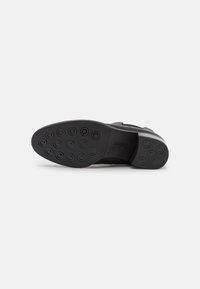 Zapato negro con una suela de goma texturizada que presenta agarraderos circulares. Material superior liso con costuras mínimas y un diseño elegante.